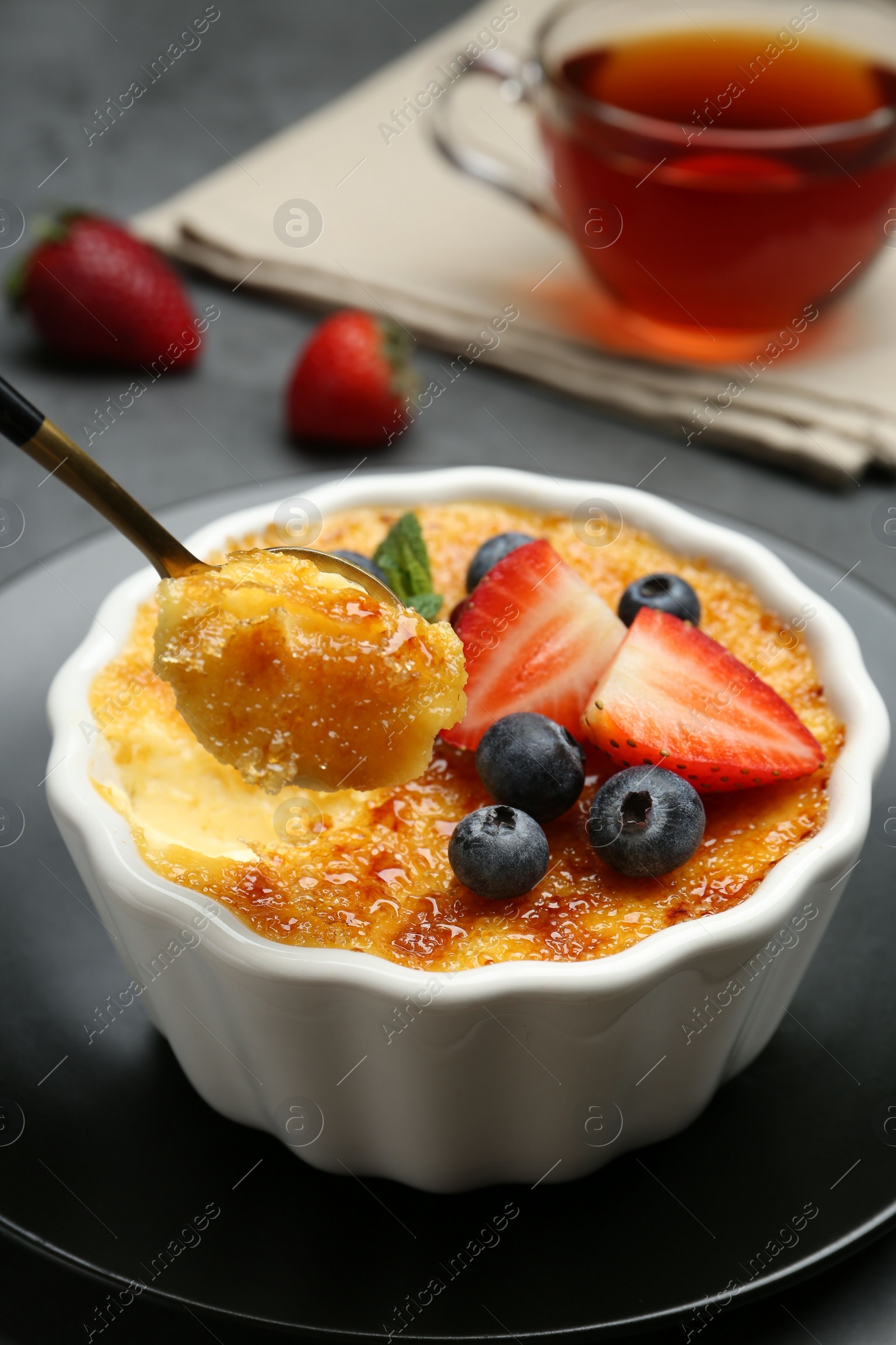 Photo of Taking delicious creme brulee with berries from bowl at grey table, closeup