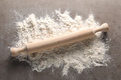 Photo of Scattered flour and rolling pin on grey textured table, top view