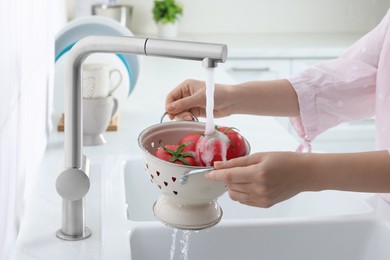Woman washing fresh ripe tomatoes under tap water in kitchen, closeup