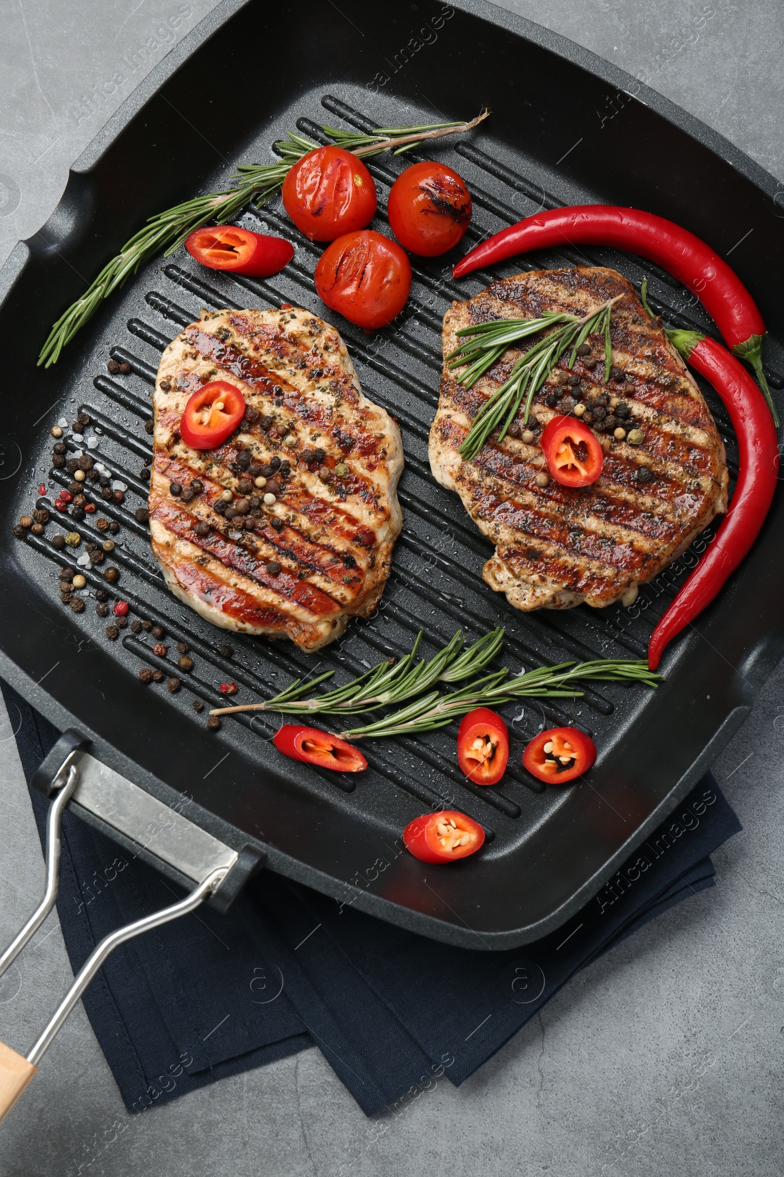 Photo of Grill pan with delicious pork steaks, spices and vegetables on grey table, top view