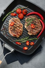 Grill pan with delicious pork steaks, spices and vegetables on grey table, top view