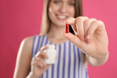 Photo of Young woman with vitamin pill against pink background, focus on hand