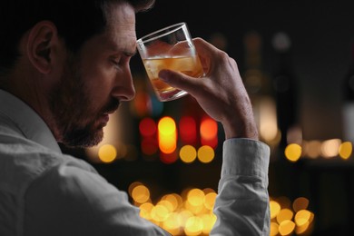 Photo of Man with glass of whiskey against blurred lights, closeup