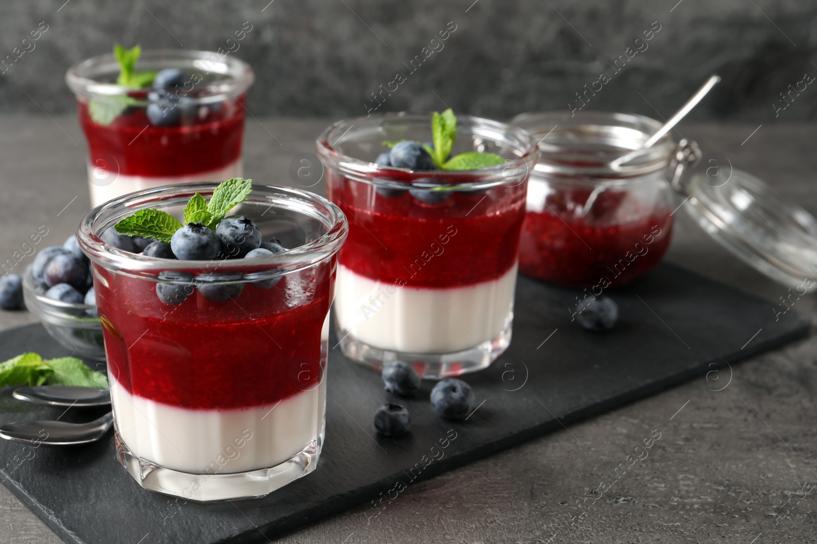 Photo of Delicious panna cotta with fruit coulis and fresh blueberries served on grey table. Space for text