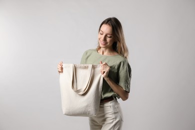 Happy young woman with blank eco friendly bag on light background