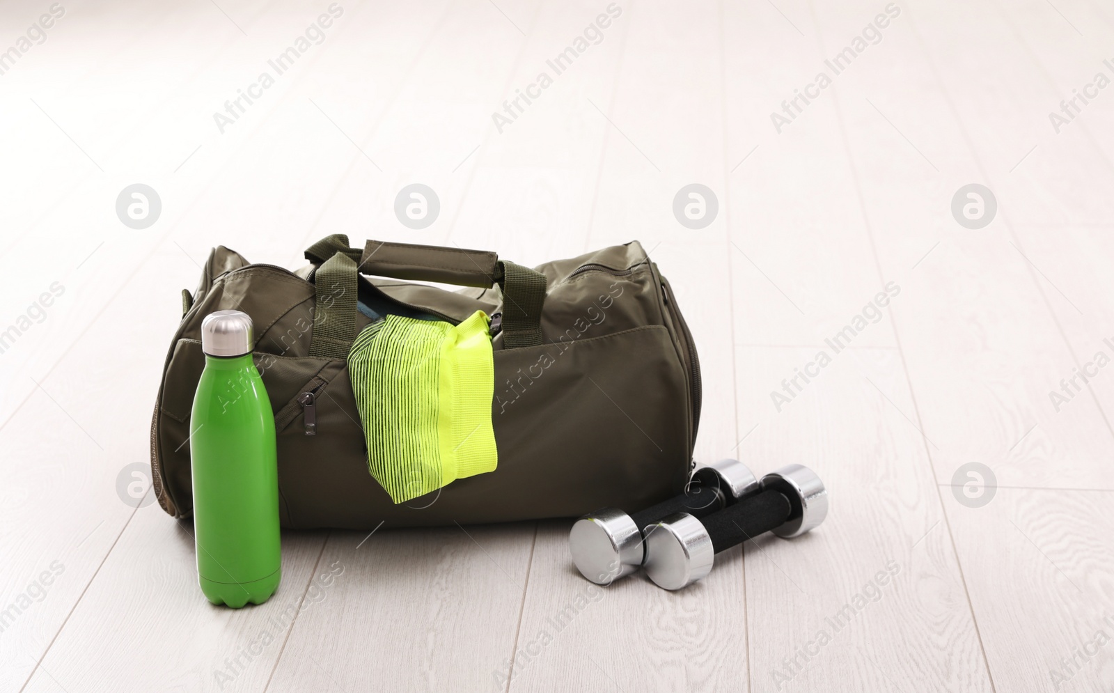 Photo of Sports bag and gym equipment on white floor. Space for text