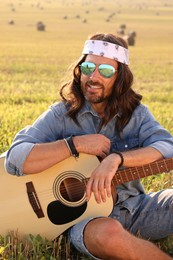 Photo of Portrait of happy hippie man with guitar in field
