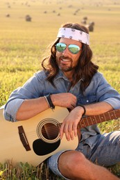 Portrait of happy hippie man with guitar in field