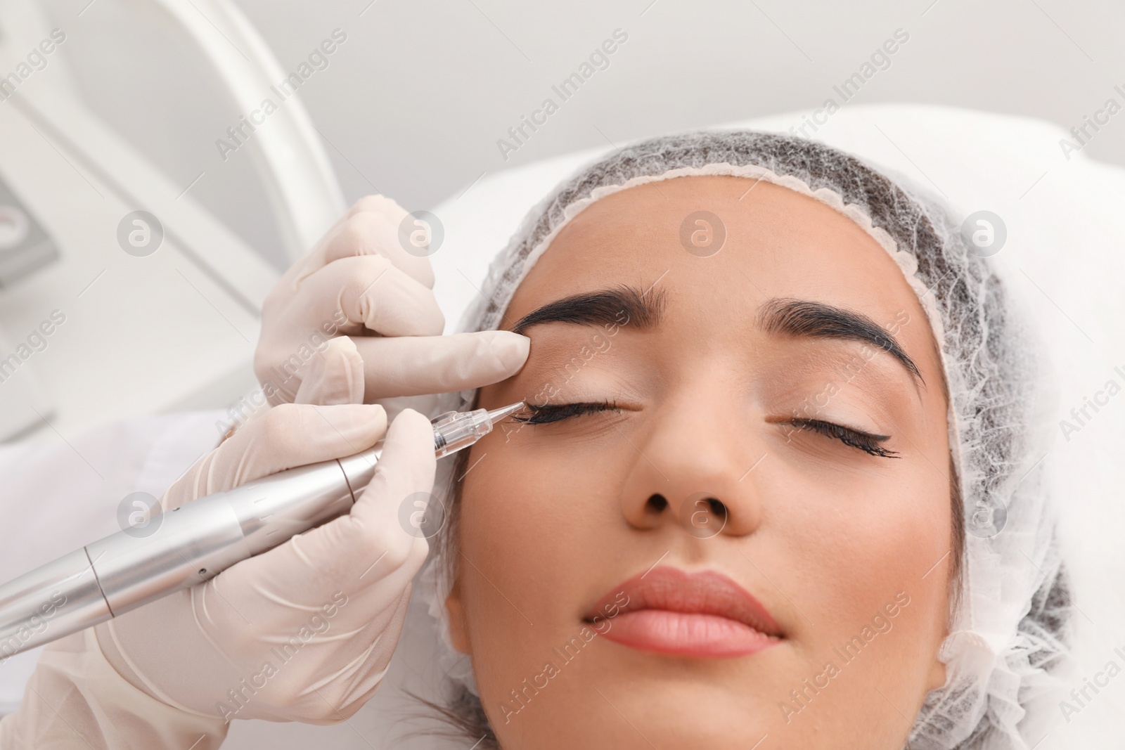 Photo of Young woman undergoing procedure of permanent eye makeup in tattoo salon, closeup