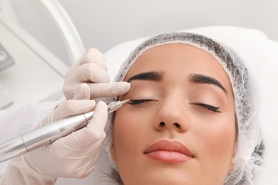 Photo of Young woman undergoing procedure of permanent eye makeup in tattoo salon, closeup