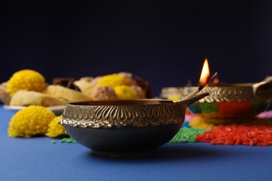 Photo of Diwali celebration. Diya lamps and colorful rangoli on blue table against violet background, closeup
