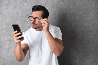 Photo of Young man with glasses using mobile phone on grey background. Vision problem