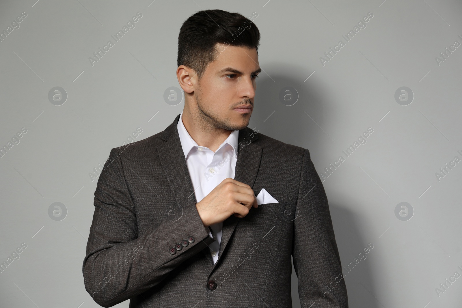 Photo of Man fixing handkerchief in breast pocket of his suit on light grey background