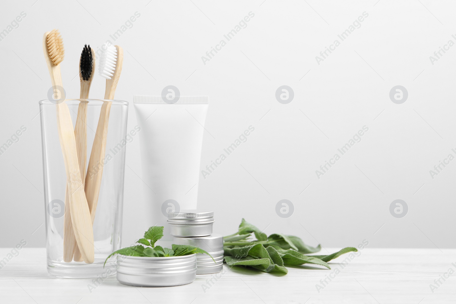 Photo of Toothbrushes, dental products and herbs on white wooden table. Space for text