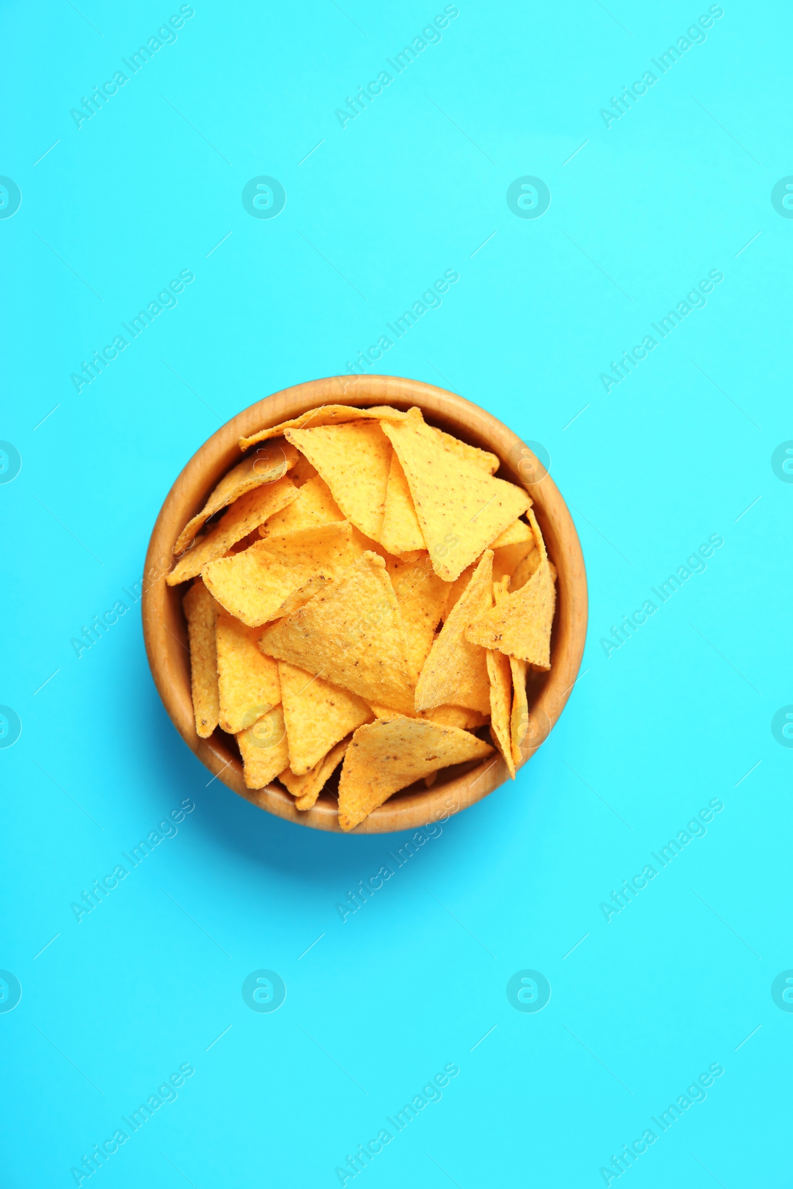 Photo of Tasty mexican nachos chips in wooden bowl on blue background, top view