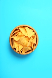 Tasty mexican nachos chips in wooden bowl on blue background, top view