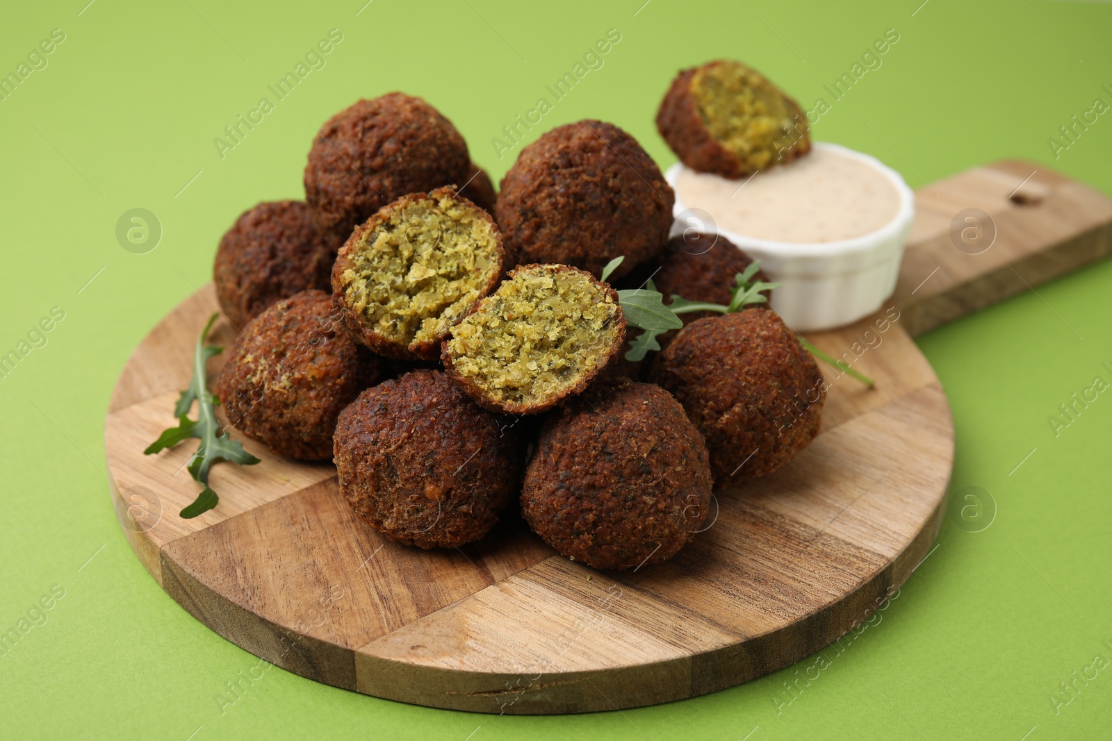 Photo of Delicious falafel balls, arugula and sauce on green background