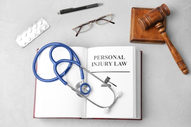 Photo of Flat lay composition with book, gavel, pills and stethoscope on grey background. Personal injury law concept