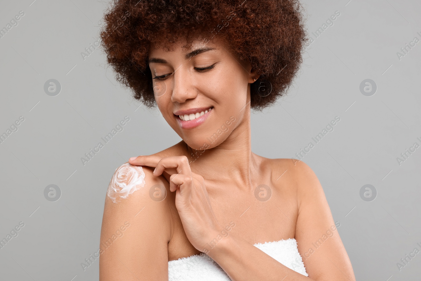 Photo of Beautiful young woman applying body cream onto shoulder on grey background