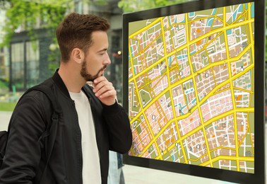 Image of Young man with backpack near public transport map at bus stop