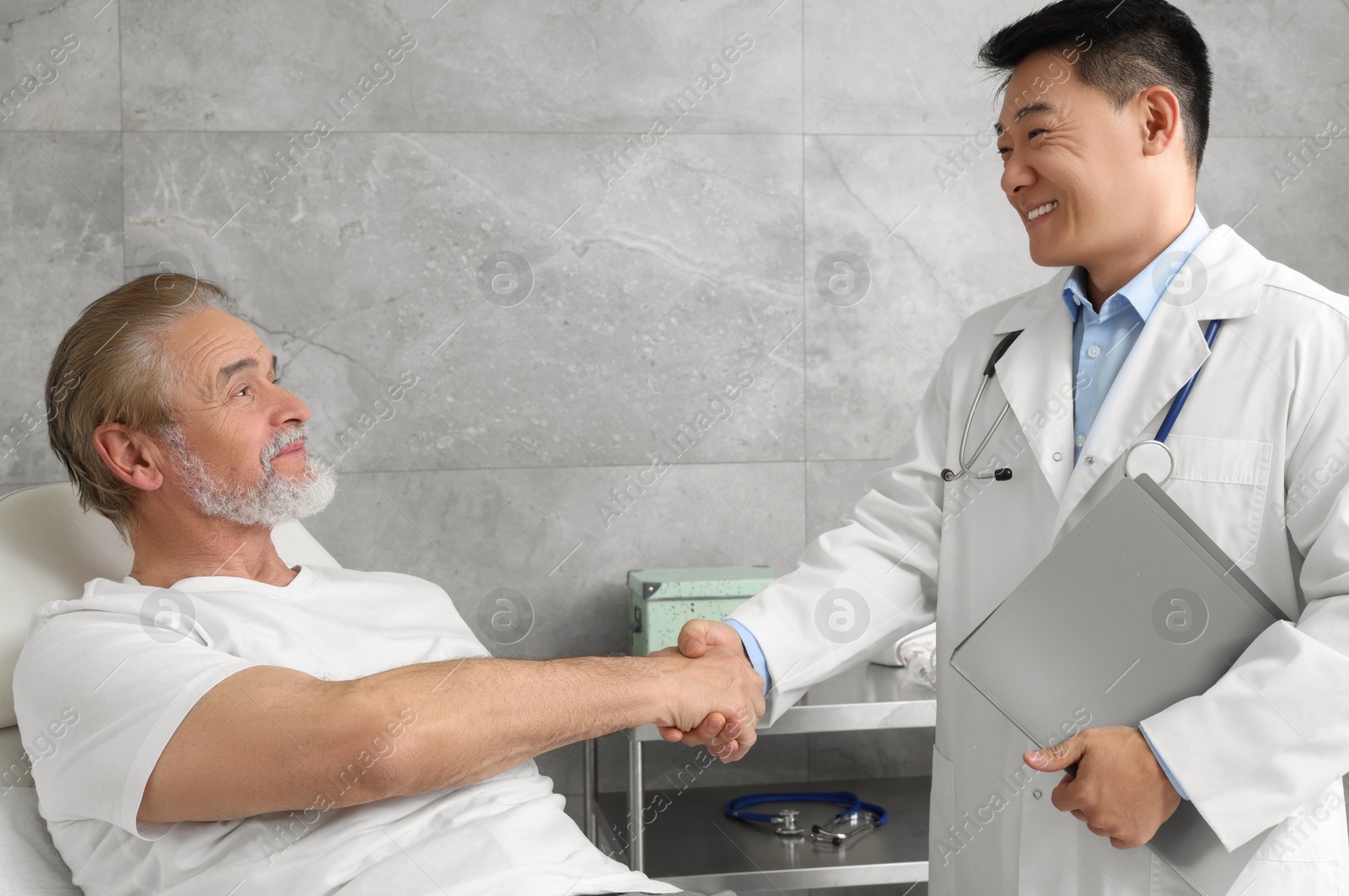 Photo of Happy doctor shaking hands with senior patient in hospital