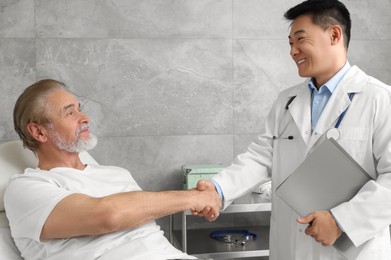 Happy doctor shaking hands with senior patient in hospital