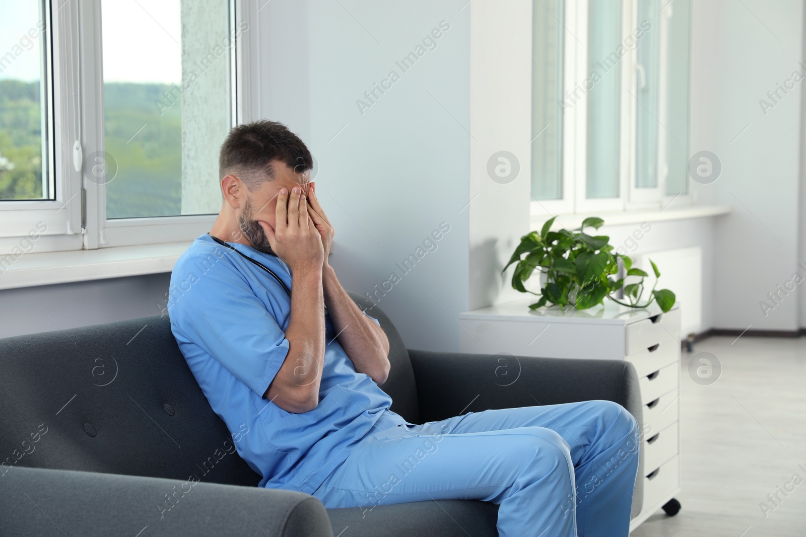 Photo of Exhausted doctor covering face on sofa in hospital