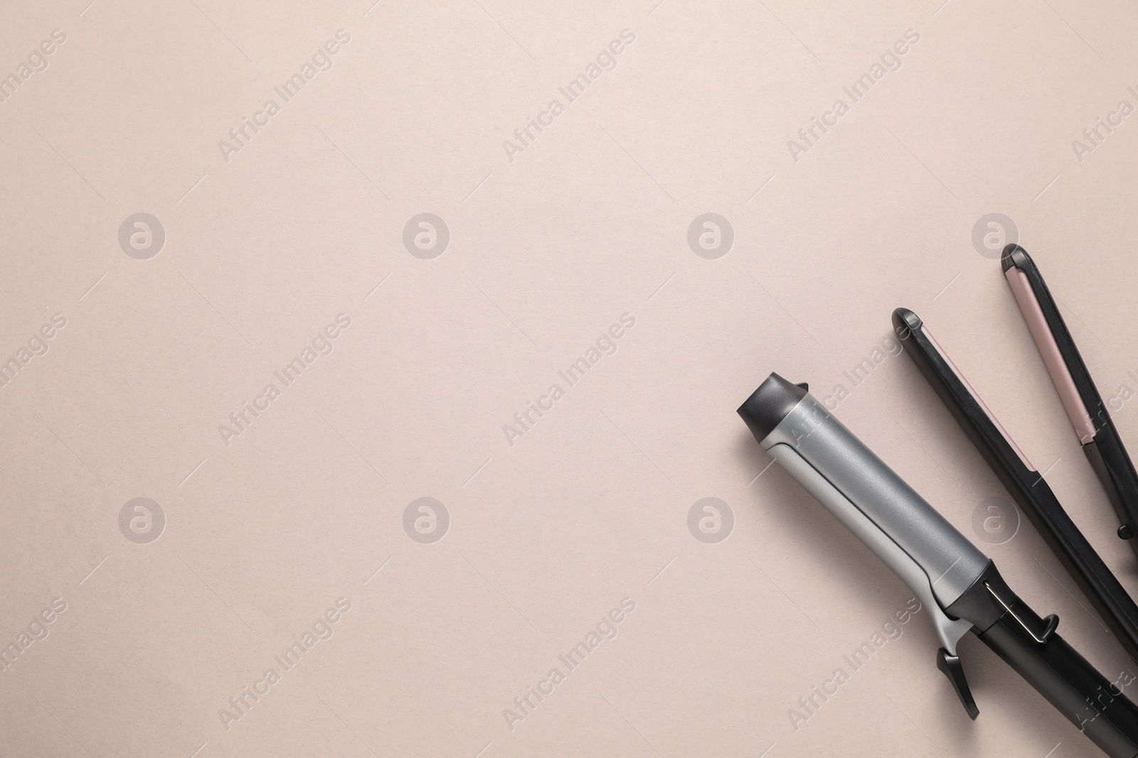 Photo of Curling iron and hair straightener on beige background, top view. Space for text