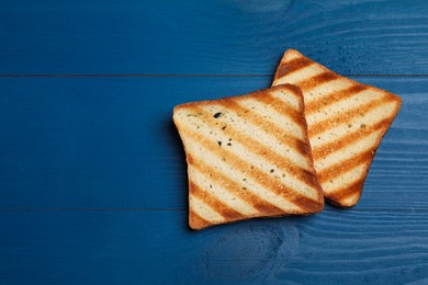 Photo of Slices of tasty toasted bread on blue wooden table, flat lay. Space for text