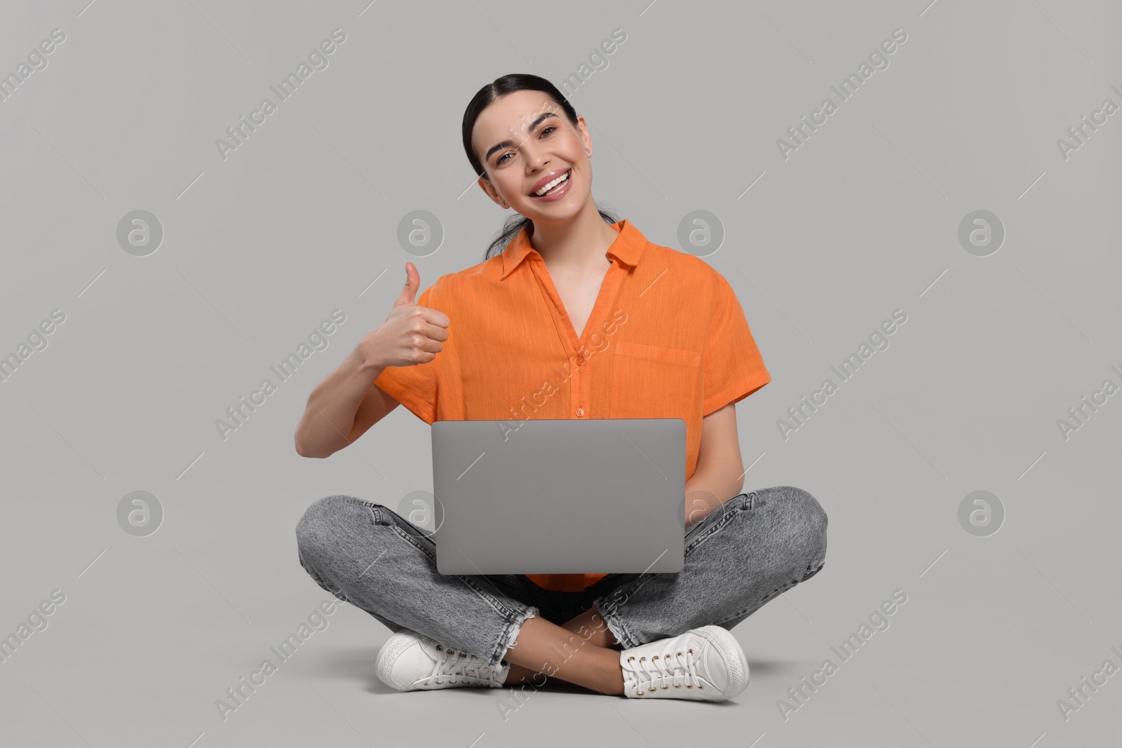 Photo of Happy woman with laptop showing thumb up on light gray background