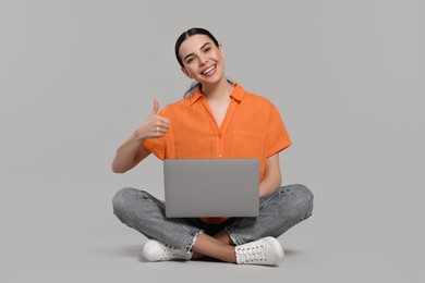 Happy woman with laptop showing thumb up on light gray background