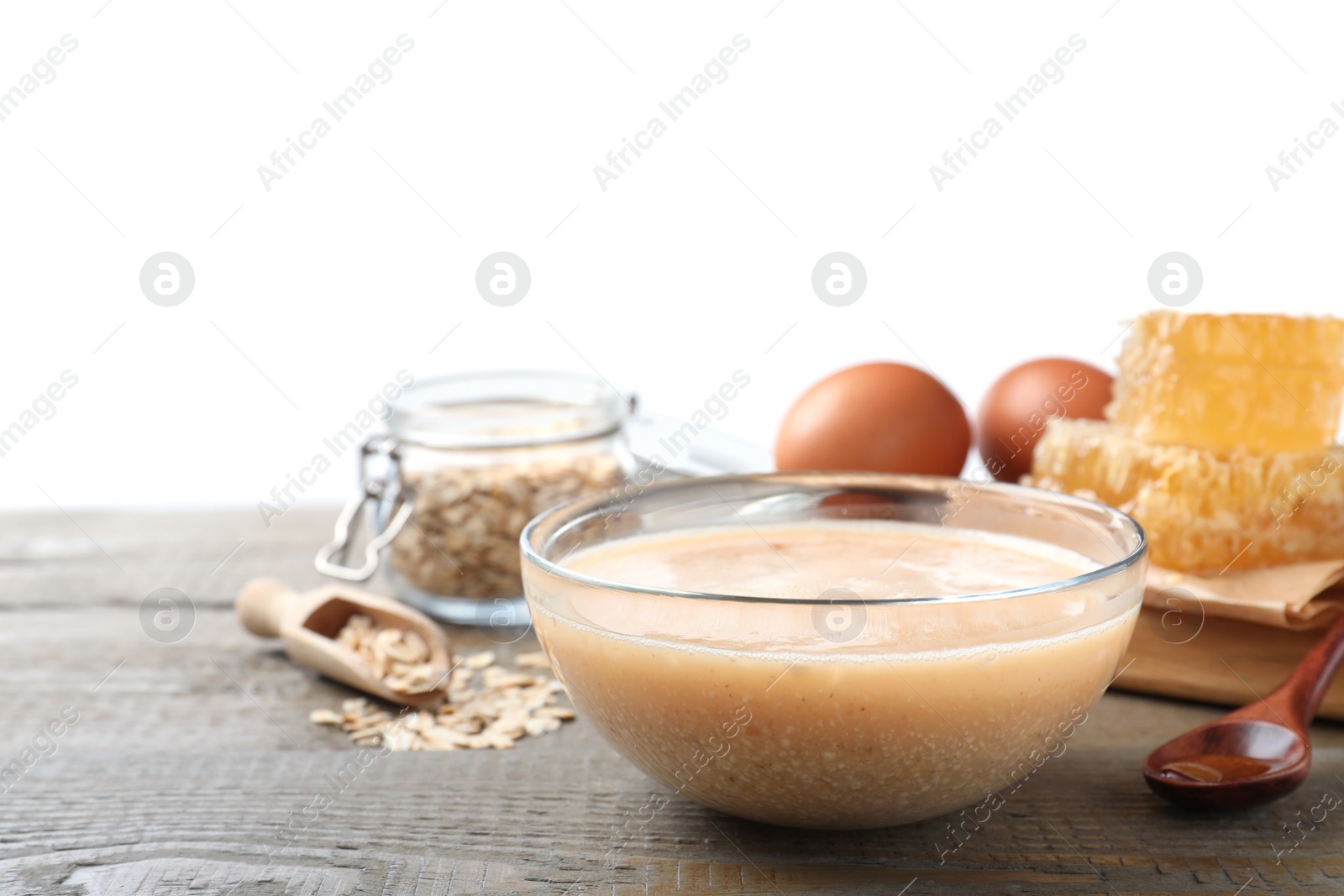 Photo of Homemade hair mask in bowl and fresh ingredients on wooden table against white background. Space for text