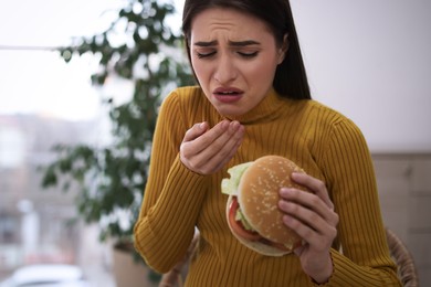 Young woman suffering from nausea while eating burger at home