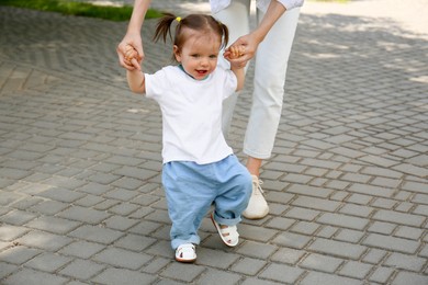 Mother supporting daughter while she learning to walk outdoors, closeup