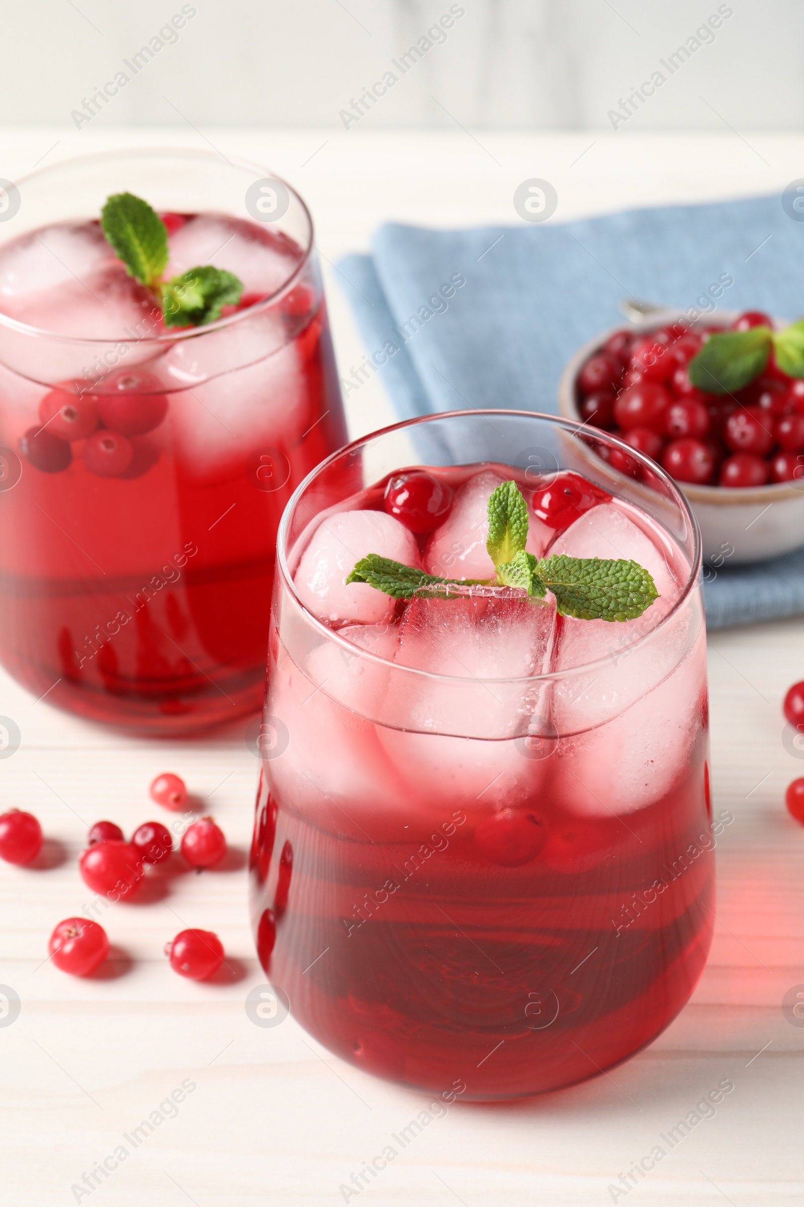 Photo of Tasty cranberry juice with ice cubes in glasses and fresh berries on white wooden table, closeup