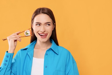 Photo of Happy beautiful young woman holding sushi roll with chopsticks on orange background. Space for text