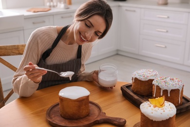 Photo of Young woman decorating traditional Easter cake with glaze in kitchen