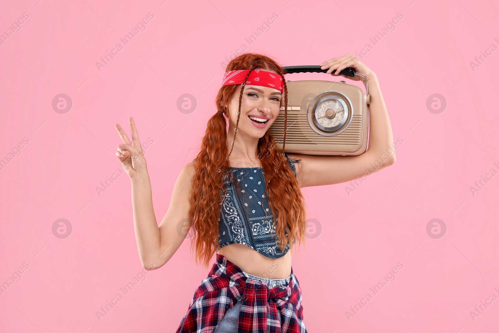 Photo of Stylish young hippie woman with retro radio receiver showing V-sign on pink background