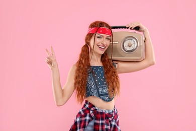 Photo of Stylish young hippie woman with retro radio receiver showing V-sign on pink background