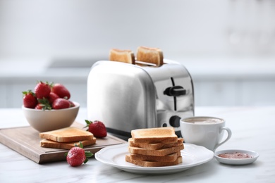 Modern toaster and tasty breakfast on white marble table in kitchen