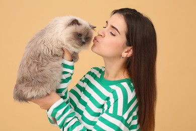 Photo of Woman kissing her cute cat on light brown background