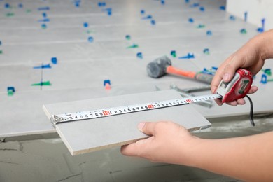 Photo of Worker measuring tile near adhesive mix on floor, closeup