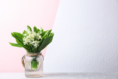 Beautiful lily of the valley bouquet in vase on table near color wall, space for text