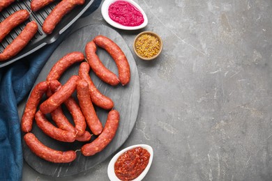 Photo of Delicious sausages, ketchup, mustard and horseradish on grey table, flat lay. Space for text