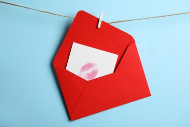 Photo of Red envelope and card with lip print hanging on twine against light blue background. Love letter