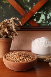 Photo of Wheat grains in bowl, spikes and flour on wooden table