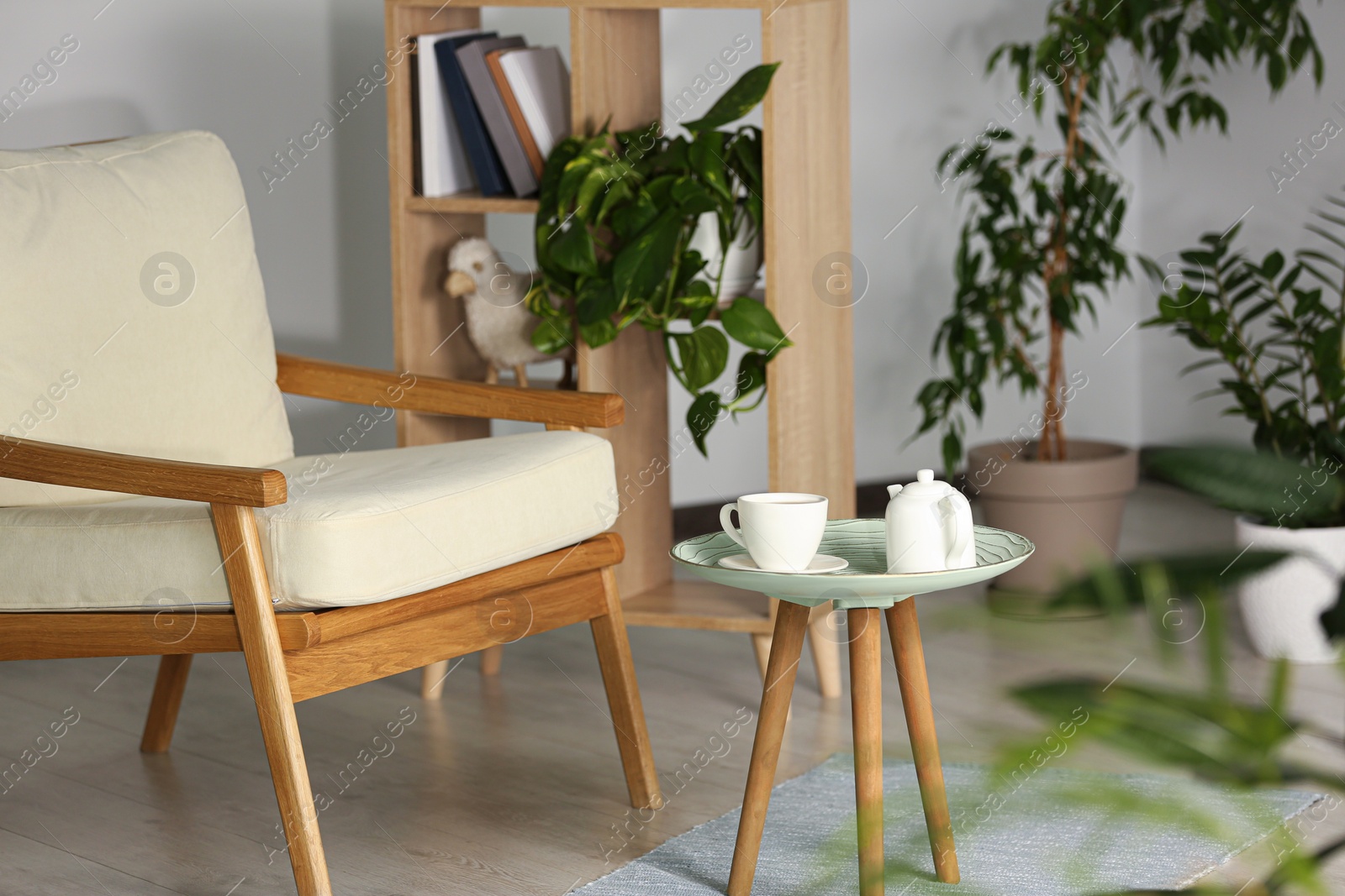 Photo of Stylish armchair, side table with cup and teapot near beautiful houseplants. Interior design
