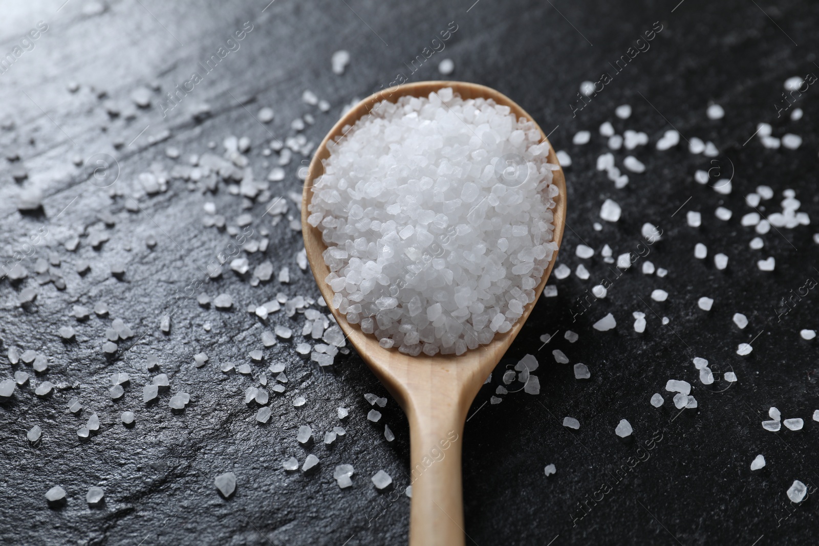 Photo of Organic white salt and spoon on black table, closeup