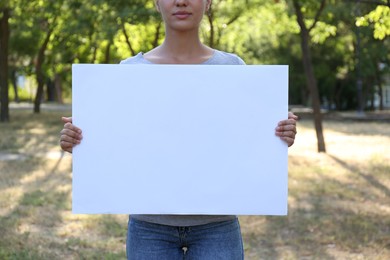 Woman holding blank poster outdoors, closeup. Mockup for design	