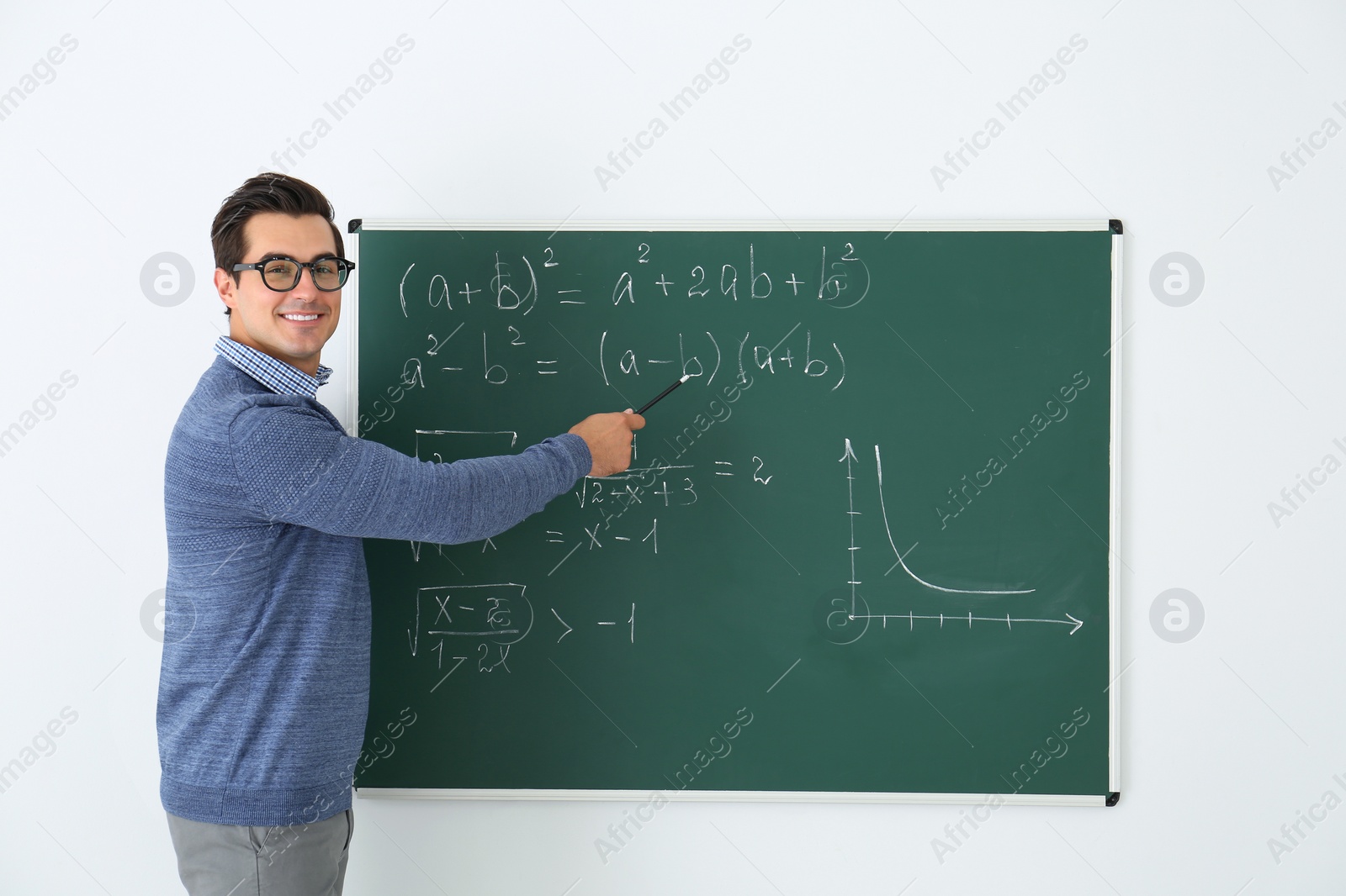 Photo of Young teacher explaining math formulas written on chalkboard in classroom